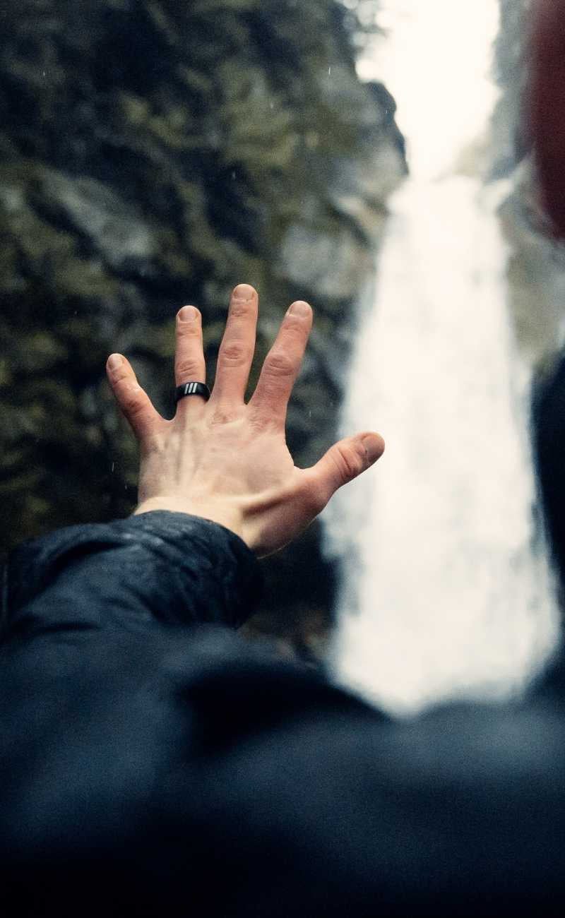 mans hand in the air by a waterfall wearing silicone rings.