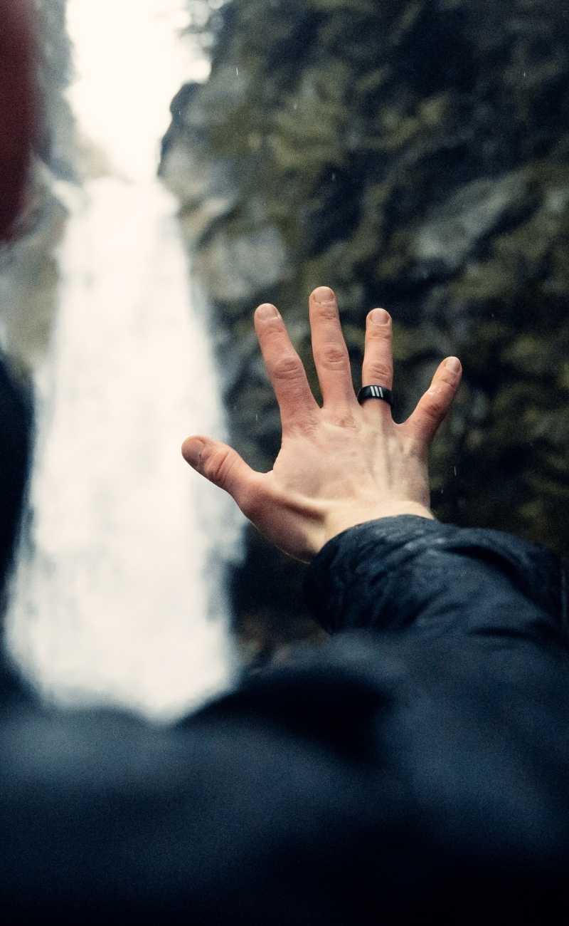 mans hand in the air by a waterfall wearing silicone rings. 